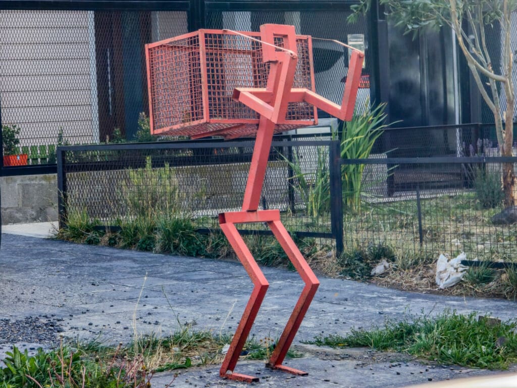 Czerwony metalowy ludzik trzymający kosz na śmieci w Río Gallegos